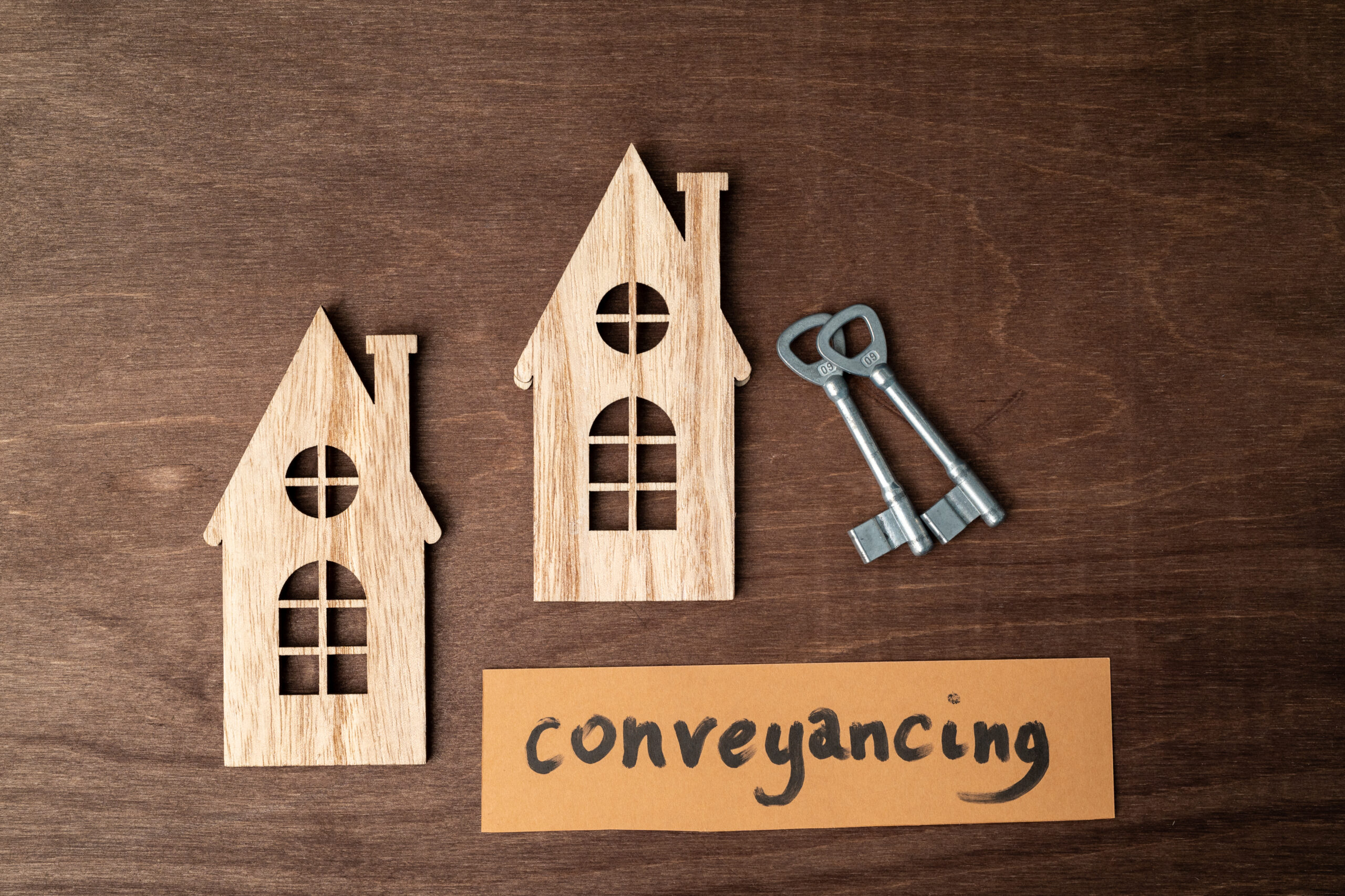 a cut out wooden house representation with a key and a card saying 'conveyancing' on wood background